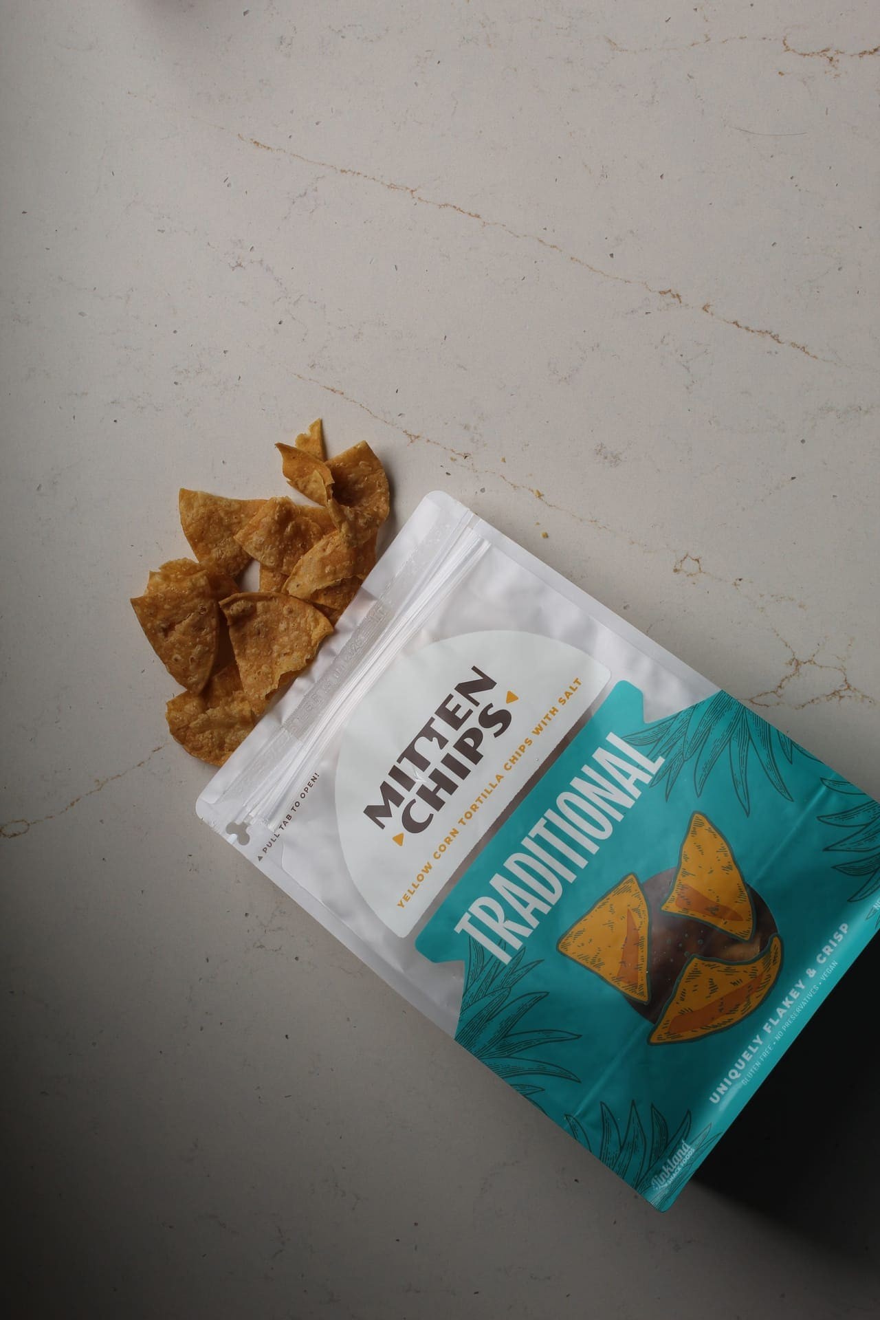 Mitten chips traditional chips on a marble table with the chips spilling out of the product bag